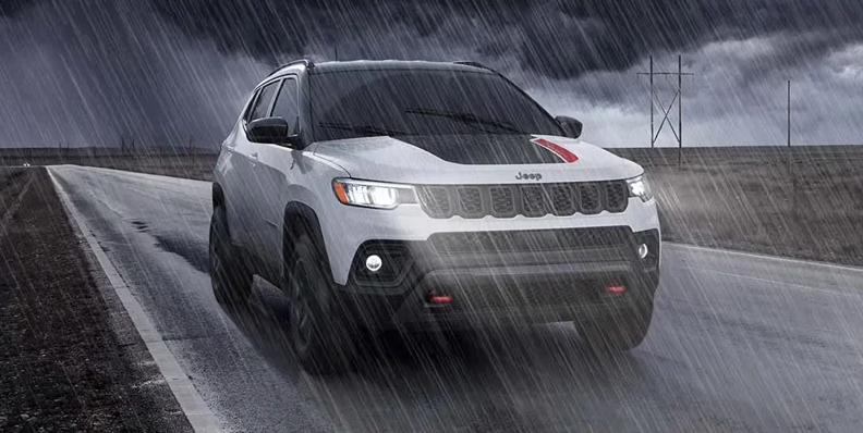 A white 2026 Jeep Compass driving down a rainy road.