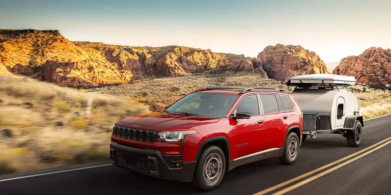 A 2026 Jeep Grand Cherokee towing a camper down the road.